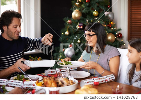 Christmas, family and parents with child in home for dinner, lunch and eating together for festival. Mother, father and girl with food for holiday, vacation and festive celebration at dining table Christmas, family and parents with child in home for dinner, lunch and eating together for festival. Mother, father and girl with food for holiday, vacation and festive celebration at dining table 141029768