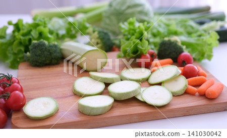 Slicing fresh young zucchini into round rings on wooden board with colorful vegetables background Slicing fresh young zucchini into round rings on wooden board with colorful vegetables background 141030042