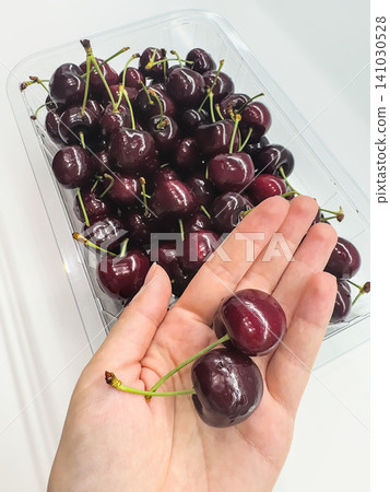 An open palm holds a few ripe cherries by a container of fruit. Sharing a healthy summer snack An open palm holds a few ripe cherries by a container of fruit. Sharing a healthy summer snack 141030528