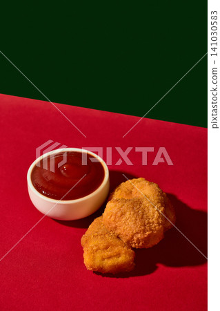 Chicken nuggets lie beside ketchup sauce on red and dark green studio background. Chicken nuggets lie beside ketchup sauce on red and dark green studio background. 141030583