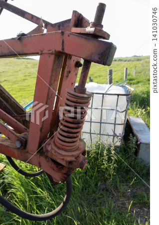 Close-up of a rusty heavy-duty coil spring on agricultural machinery with green farmland in the background Close-up of a rusty heavy-duty coil spring on agricultural machinery with green farmland in the background 141030746