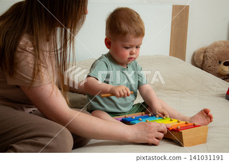 Toddler striking xylophone bars with mallet. Hand eye coordination meets music learning. Age appropriate development of hearing and finger control. Playful education in action 141031191