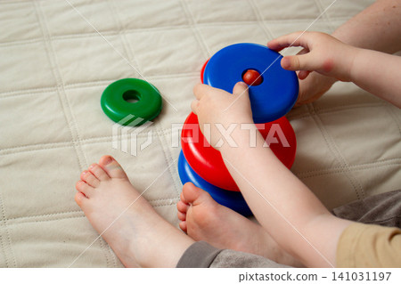 Two year old focusing on ring stacking playing with plastic pyramid toy. Logic and thinking skills growth. Bright colors attract attention. Fine motor practice 141031197