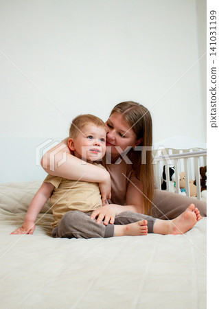 Two years old boy and his mom lying on bed together laughing, playing and having fun. Heartwarming display of mother son connection Two years old boy and his mom lying on bed together laughing, playing and having fun. Heartwarming display of mother son connection 141031199