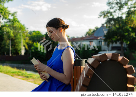 Woman reading in sunlit park. No smartphone. Cognitive refresh through pages. Self education in priority. Celebrating August 9 book lovers day 141031274