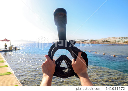 Woman holding a snorkeling mask up against the bright blue sky with the sea in the background Woman holding a snorkeling mask up against the bright blue sky with the sea in the background 141031372
