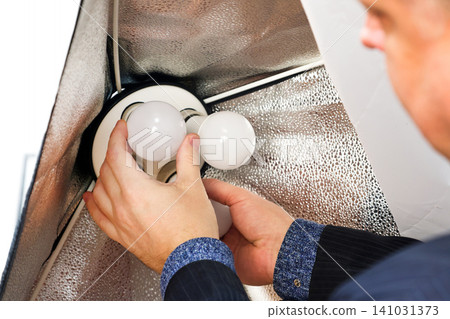 Male photographer screwing a light bulb into a softbox in a professional photography studio, Close-up Male photographer screwing a light bulb into a softbox in a professional photography studio, Close-up 141031373