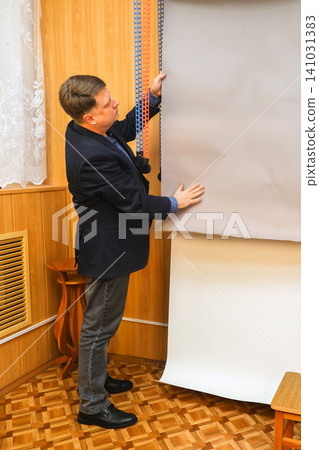 A male photographer lowers a gray paper backdrop in a professional studio A male photographer lowers a gray paper backdrop in a professional studio 141031383