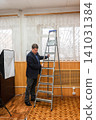 Male photographer carrying a tall portable ladder to replace a burnt-out light bulb on the studio ceiling 141031384