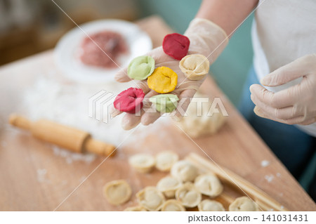 Woman in gloves holding colorful handmade dumplings over a kitchen table Woman in gloves holding colorful handmade dumplings over a kitchen table 141031431