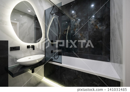 Modern luxury bathroom with black marble accents and backlit organic mirror Modern luxury bathroom with black marble accents and backlit organic mirror 141031485