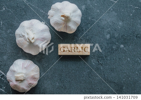 Flat lay top view of three fresh white garlic bulbs next to an engraved wooden block with text on a dark gray marble background with copy space Flat lay top view of three fresh white garlic bulbs next to an engraved wooden block with text on a dark gray marble background with copy space 141031709