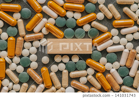 Top view pattern of colorful pharmaceutical pills and dietary supplement capsules arranged around a blank rectangular wooden block for copy space text Top view pattern of colorful pharmaceutical pills and dietary supplement capsules arranged around a blank rectangular wooden block for copy space text 141031743