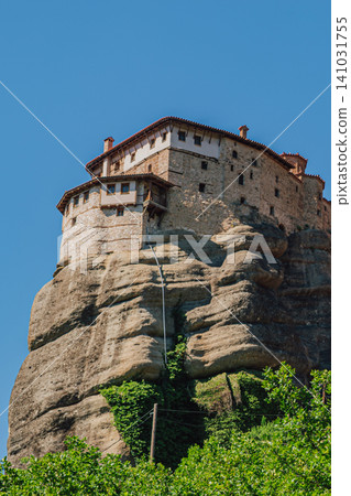 Vertical close up shot of a historic stone orthodox monastery building standing on a high sandstone cliff edge with green climbing ivy on a bright sunny day Vertical close up shot of a historic stone orthodox monastery building standing on a high sandstone cliff edge with green climbing ivy on a bright sunny day 141031755