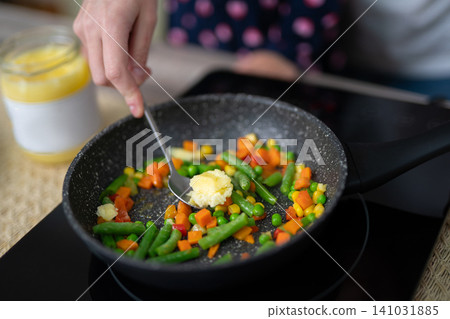 Woman adding ghee butter to a vegetable stir-fry in a frying pan Woman adding ghee butter to a vegetable stir-fry in a frying pan 141031885