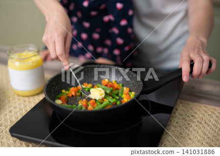 Woman adding ghee butter to a vegetable stir-fry in a frying pan Woman adding ghee butter to a vegetable stir-fry in a frying pan 141031886