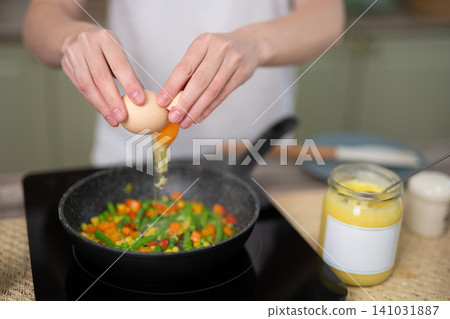 Woman cracking an egg over a vegetable stir-fry in a frying pan Woman cracking an egg over a vegetable stir-fry in a frying pan 141031887