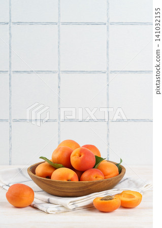 Fresh ripe apricots in wooden bowl on white kitchen table and white tiled wall with copy space 141032155