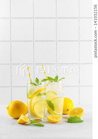 Fresh homemade lemonade with lemon slices, mint and ice in glasses on white kitchen tile background Fresh homemade lemonade with lemon slices, mint and ice in glasses on white kitchen tile background 141032156