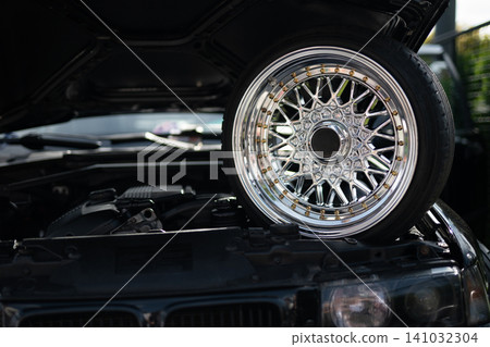 Custom chrome wire wheel and engine bay of a classic black car Custom chrome wire wheel and engine bay of a classic black car 141032304