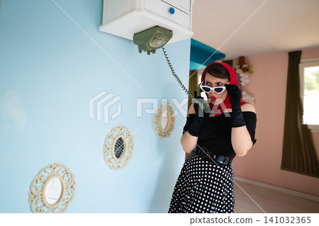 a girl retro style, speaks by phone, in an upside-down house, as well as furniture placed on the up a girl retro style, speaks by phone, in an upside-down house, as well as furniture placed on the up 141032365