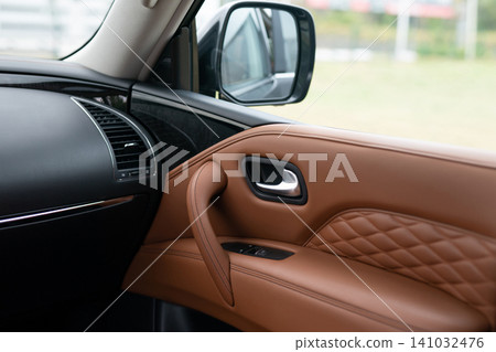 Interior view of a luxury SUV passenger door panel and brown leather trim 141032476