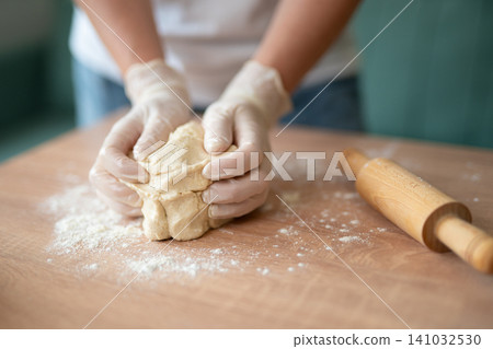 Hands in gloves kneading fresh dough on a floured wooden table Hands in gloves kneading fresh dough on a floured wooden table 141032530