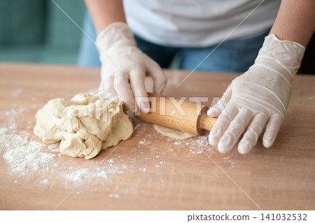Woman in gloves using rolling pin on fresh dough on wooden table Woman in gloves using rolling pin on fresh dough on wooden table 141032532