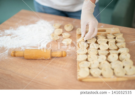 Woman in gloves arranging handmade dumplings on a wooden board Woman in gloves arranging handmade dumplings on a wooden board 141032535