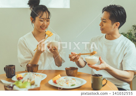 A scene of a couple eating tamagoyaki (Japanese rolled omelet) and rice at a dining table, chatting and smiling. A scene of a couple eating tamagoyaki (Japanese rolled omelet) and rice at a dining table, chatting and smiling. 141032555