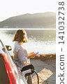 Woman traveler with charging plug next to her electric car on the sea coast at sunset 141032738