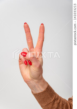 Female hand with red nail polish forming a V sign for peace or victory, two fingers raised against a clean white studio background, communicating success or counting two Female hand with red nail polish forming a V sign for peace or victory, two fingers raised against a clean white studio background, communicating success or counting two 141033213
