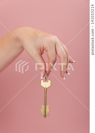 Woman's hand offering a golden house key on a pink background, symbolizing new beginnings, property ownership, security, and access to a dream home Woman's hand offering a golden house key on a pink background, symbolizing new beginnings, property ownership, security, and access to a dream home 141033214