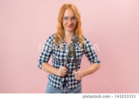 Young woman wearing a plaid shirt and safety glasses, confidently holding a large pipe wrench, embodying strength and capability for home improvement and skilled work 141033333