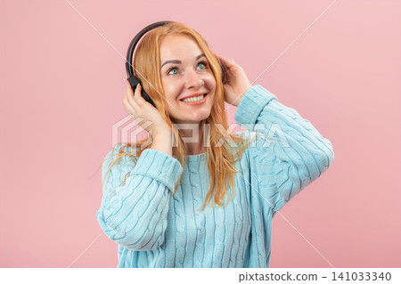 Young woman smiling while listening to her favorite audio content on headphones, expressing joy and inspiration against a solid pink background Young woman smiling while listening to her favorite audio content on headphones, expressing joy and inspiration against a solid pink background 141033340