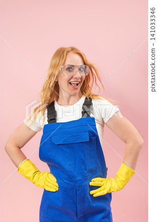 Cheerful red haired woman with safety goggles and yellow gloves standing confidently with hands on hips, expressing excitement and readiness for work against a pink background Cheerful red haired woman with safety goggles and yellow gloves standing confidently with hands on hips, expressing excitement and readiness for work against a pink background 141033346