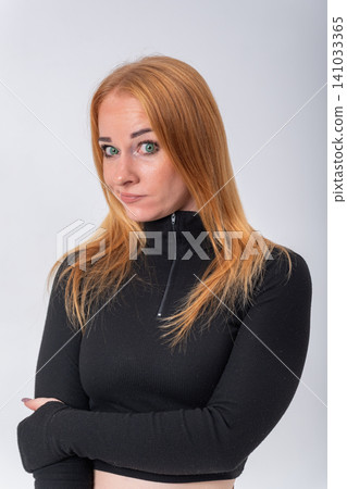 Young woman posing in studio against a clear background, crossing her arms and making a face conveying curiosity, mild skepticism, or thoughtful consideration Young woman posing in studio against a clear background, crossing her arms and making a face conveying curiosity, mild skepticism, or thoughtful consideration 141033365