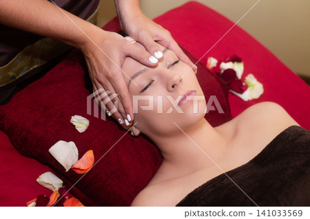 a masseuse in a cosmetology salon makes a Thai massage on the face of a young girl a masseuse in a cosmetology salon makes a Thai massage on the face of a young girl 141033569