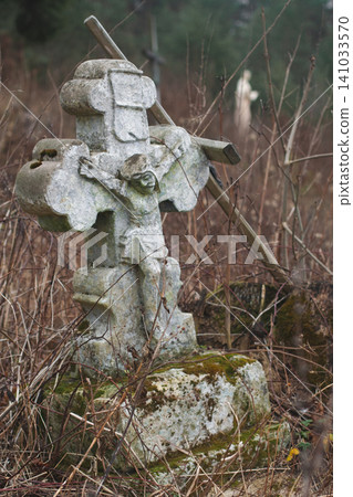 Ancient mossy stone crucifix monument standing among bare branches in a quiet winter forest 141033570