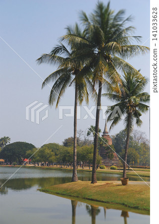 Tropical palm trees and ancient Buddhist stupa by a pond in Sukhothai Tropical palm trees and ancient Buddhist stupa by a pond in Sukhothai 141033628