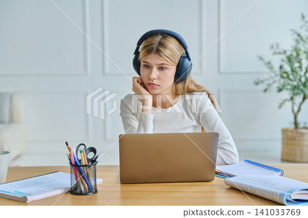 Bored teenage girl in headphones looking at laptop Bored teenage girl in headphones looking at laptop 141033769