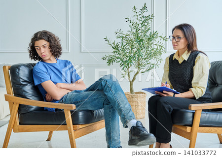 Depressed teenager ignoring female psychologist in office session Depressed teenager ignoring female psychologist in office session 141033772