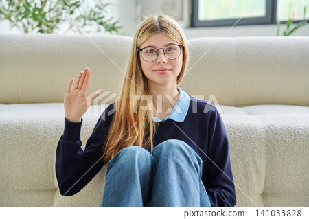 Smiling teenage girl in glasses waving hand during online video call. 141033828