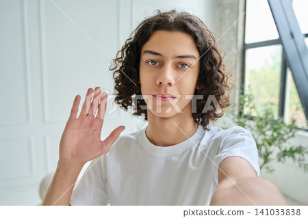 Teen boy taking selfie and waving hand in greeting Teen boy taking selfie and waving hand in greeting 141033838