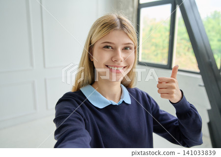 Happy young woman taking selfie showing thumbs up Happy young woman taking selfie showing thumbs up 141033839