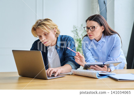 Teenage student and teacher looking at laptop indoor Teenage student and teacher looking at laptop indoor 141034065