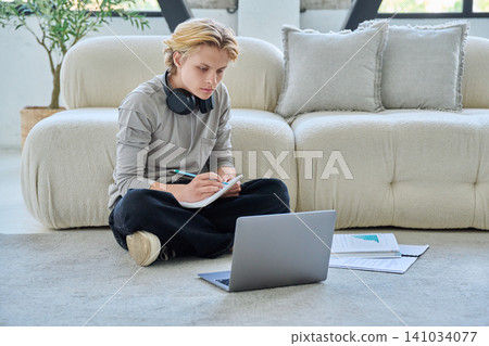 Young student studying with laptop on floor at home Young student studying with laptop on floor at home 141034077