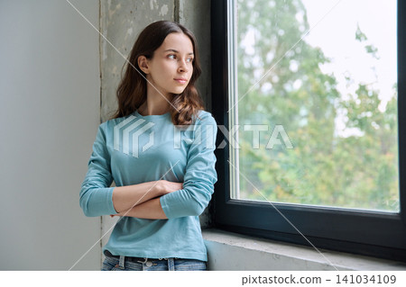 Pensive teen girl with crossed arms looking out window Pensive teen girl with crossed arms looking out window 141034109