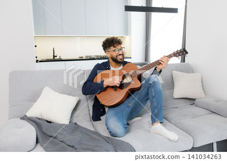 Happy man playing acoustic guitar on sofa 141034263