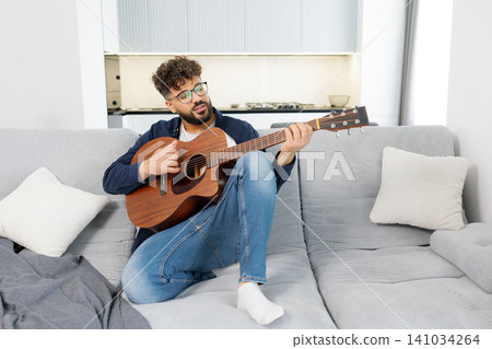 Man playing acoustic guitar and singing on sofa 141034264